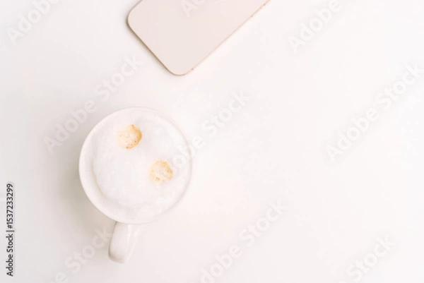 Fototapeta Top view of cappuccino with two espresso spots and beige phone on a white surface. High quality photo