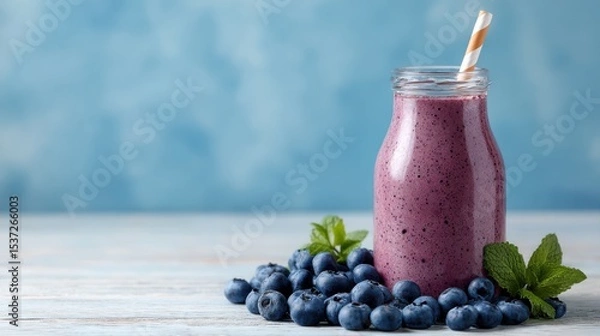 Fototapeta A refreshing blueberry smoothie is presented in a glass jar, surrounded by fresh blueberries and sprigs of mint. Soft blue background enhances the colorful drink