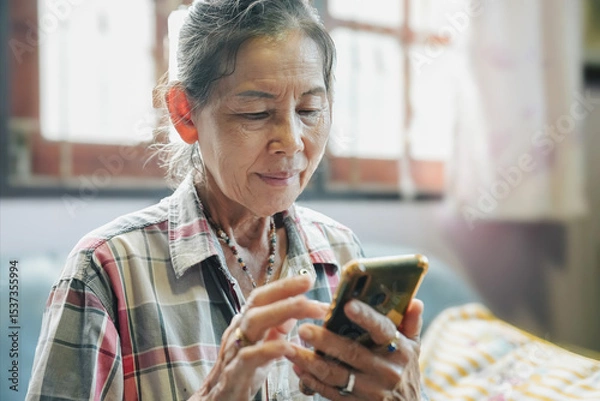 Obraz An elderly woman engages with her smartphone, highlighting technology's role in modern daily life.
