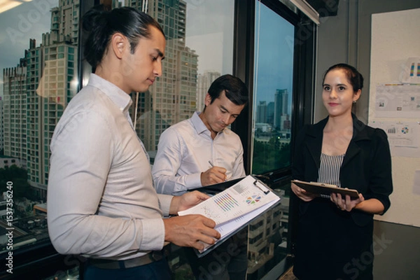 Obraz Three professionals collaborate in a modern office environment, engaging in discussion and planning.
