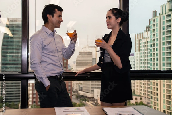 Obraz Two professionals enjoy cocktails while discussing ideas in a modern office overlooking the city skyline.