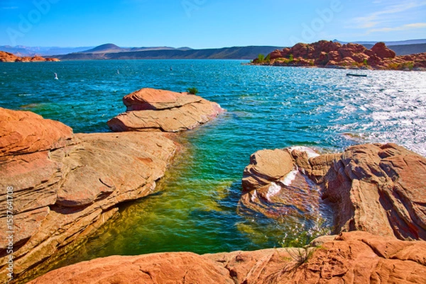 Fototapeta Red Sandstone and Blue Lake Water with Distant Hills Low Angle Lake Edge