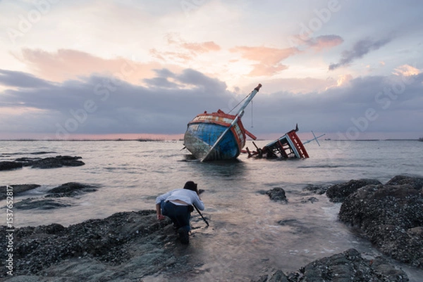 Fototapeta Old wrecked fishing boat at shore of Ang Sila Village, Chonburi Province of thailand with sunset skyline and clouds background. Include photographer to shoot for beautiful landscape at twilight.