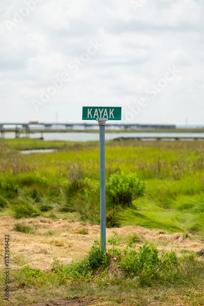 Obraz A street sign in the grass with water and a bridge in the background. 