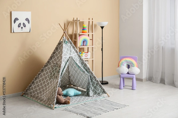 Fototapeta Interior of children's room with play tent, lamp, chair and many toys in shelving unit near beige wall