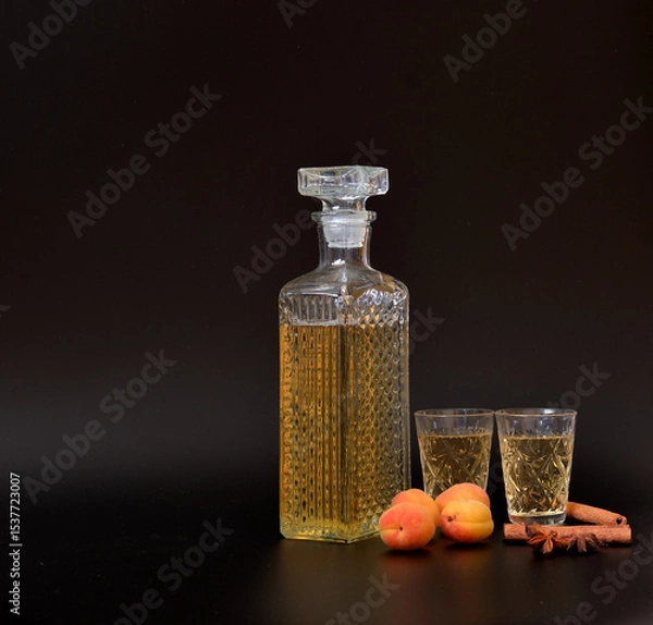 Obraz Apricot liqueur with anise and cinnamon in a crystal decanter and two glasses on a black background.