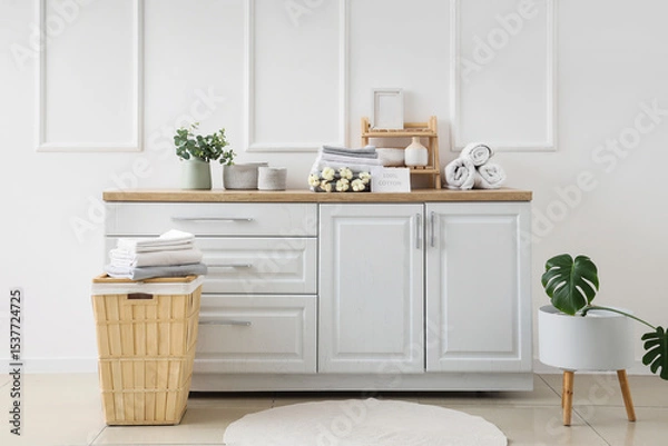 Fototapeta Interior of bathroom with clean bed sheets stacks, cotton flowers sprig and home decor on table in room