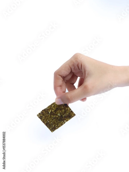 Fototapeta Hand holding a square sheet of roasted seaweed snack against a white background.