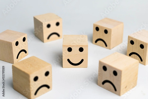 Fototapeta happy face in the center among sad face expression emoji on wooden blocks isolated on white background