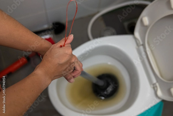 Fototapeta A woman's hand is using an air pump to solve a clogged toilet.