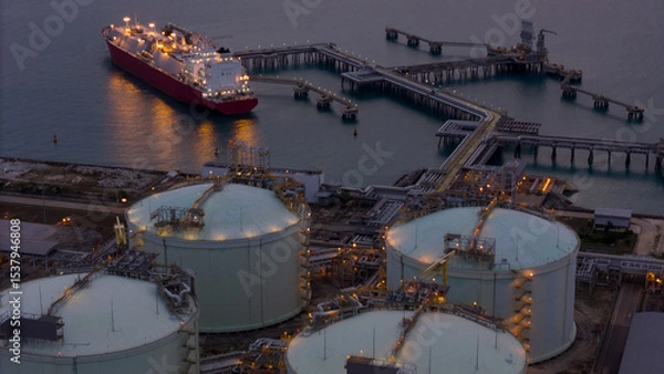 Obraz Aerial view of an LNG tanker docked at an offshore terminal with multiple pipelines, storage tanks, and an industrial complex. Captures global energy logistics