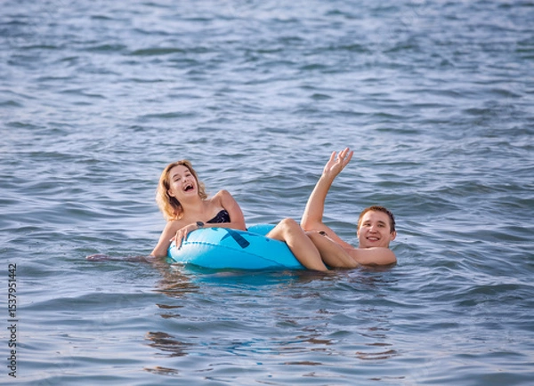 Fototapeta A cheerful young couple swims in the sea with an inflatable circle