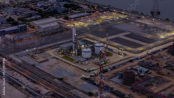 Obraz large industrial oil and gas storage tanks at a coastal refinery terminal during dusk. Tanker ships docked at long piers highlight the global energy transport infrastructure.
