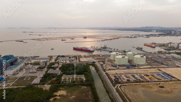 Obraz Aerial view of an LNG tanker docked at an offshore terminal with multiple pipelines, storage tanks, and an industrial complex. Captures global energy logistics