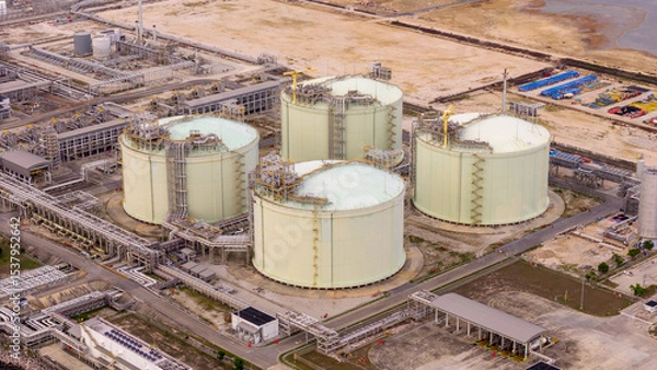Obraz LNG storage tanks and terminal facility at dusk, showcasing large cylindrical containers, offshore piers, and cargo ships. Industrial landscape representing global liquefied natural gas