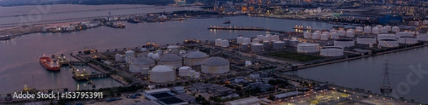 Obraz large industrial oil and gas storage tanks at a coastal refinery terminal during dusk. Tanker ships docked at long piers highlight the global energy transport infrastructure.