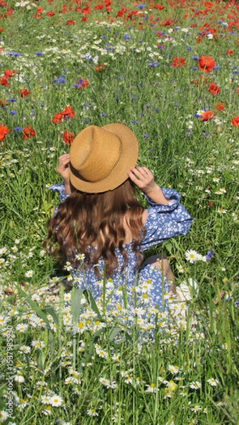 Obraz Woman Enjoying a Sunny Day in a Blooming Wildflower Field Wearing a Straw Hat and a Blue Dress With Floral Patterns