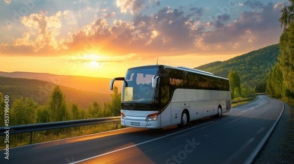 Obraz A white bus travels along an asphalt road surrounded by a line of trees in a rural landscape at sunset, with distant mountains visible. A scenic and peaceful countryside transportation scene.
