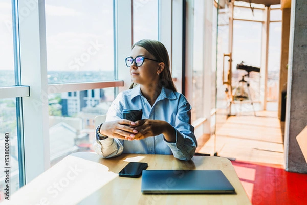 Fototapeta A thoughtful young professional is situated in a modern workspace, fully engaged while manipulating both a smartphone and a laptop, embodying the essence of productivity and innovation