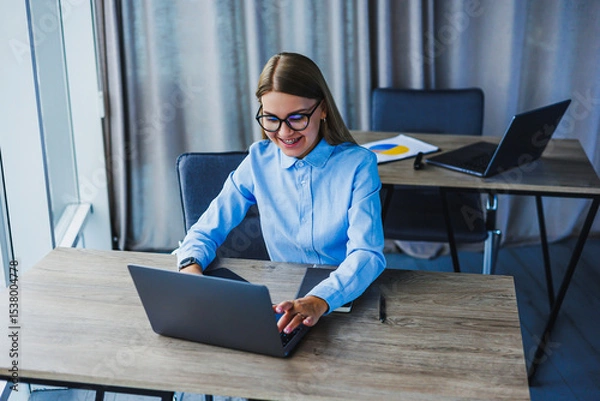 Fototapeta A young professional is currently engaged in remote work, showcasing a modern home office setup that is situated in a bright, minimalistic environment, which enhances focus and creativity