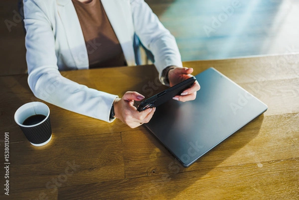 Fototapeta In a modern workspace, a focused professional woman adeptly uses her smartphone and laptop while enjoying coffee, highlighting her impressive multitasking skills in todays fastpaced work life