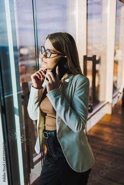 Fototapeta A professional businesswoman is deeply engaged in an important phone call in a modern office, characterized by stunning views of the city skyline that inspire productivity and innovation