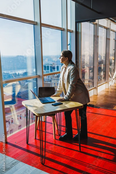 Fototapeta A dedicated business professional gazes out at the skyline from their office, reflecting their aspirations, ambition, and strong motivation to succeed and achieve their career goals