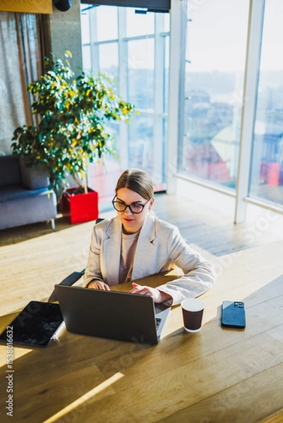 Fototapeta A dedicated professional woman is focused on working diligently on her laptop while seated in a modern office environment, showcasing her commitment to her tasks and responsibilities