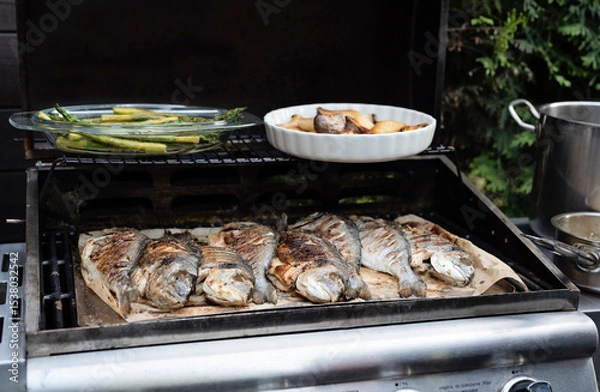 Fototapeta Grilled fish on the grill. Delicious sea bream with asparagus ready to eat for lunch or main dinner. Preparing and grilling during garden party. Cookout. Close up.