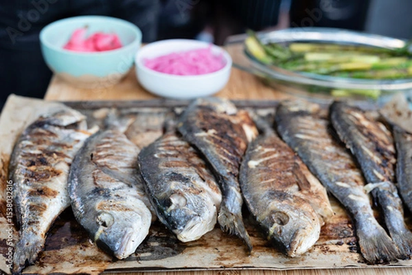 Fototapeta Grilled fish with vegetables as a mediterranean meal ready to eat. Dorada fish on a board made during barbecue on grill. Delicious healthy food for lunch or main dinner. Close up.