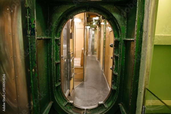 Obraz A narrow corridor inside a U.S. Navy submarine is viewed through a green-painted metal hatch. The hallway is lined with doors and bunks, showing the compact layout of the crew area.