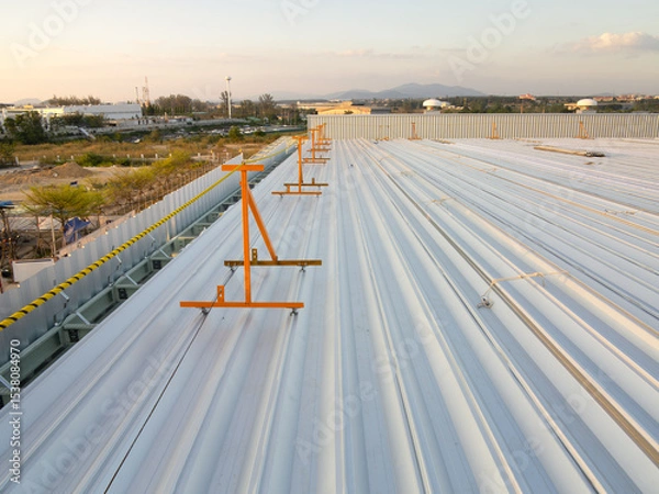 Fototapeta Metal roof sheet installation work for factory warehouse construction project site with sky background at evening. Include safety equipment tool or guard rail and rope for prevent worker falling from