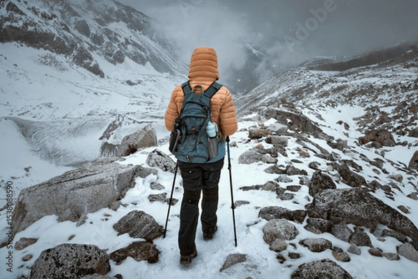 Fototapeta Hiker walks along snowy trail through mountain pass against backdrop of an approaching snow storm in Himalayas.