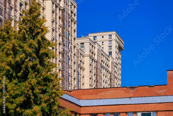 Obraz City view on a sunny day. Modern building and houses against the blue sky.