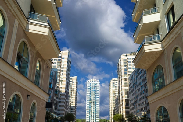 Obraz City view on a sunny day. Modern building and houses against the blue sky.