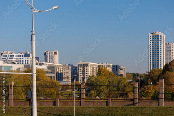 Obraz City view on a sunny day. Modern building and houses against the blue sky.