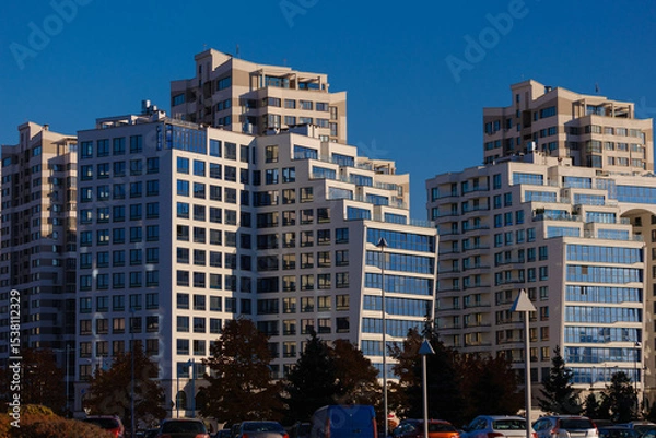 Obraz City view on a sunny day. Modern building and houses against the blue sky.