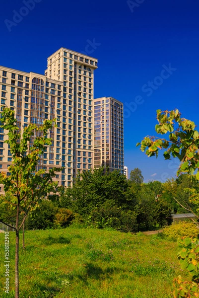 Obraz City view on a sunny day. Modern building and houses against the blue sky.