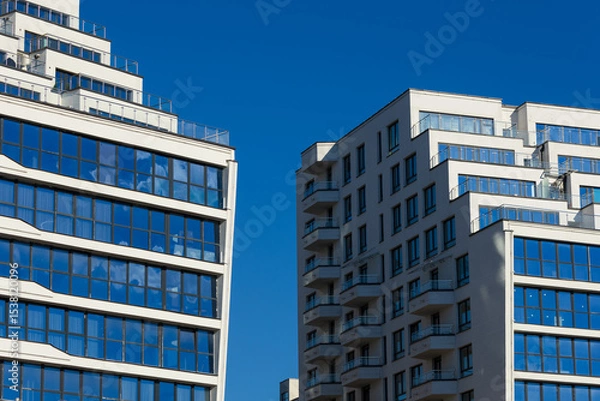 Obraz City view on a sunny day. Modern building and houses against the blue sky.