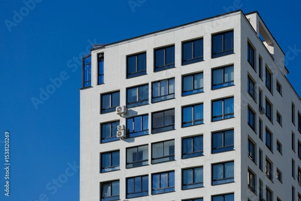 Obraz City view on a sunny day. Modern building and houses against the blue sky.