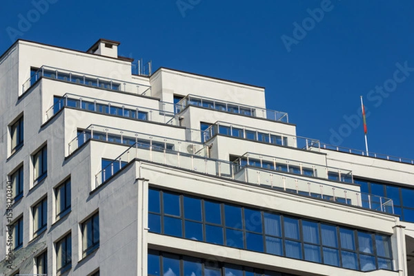 Obraz City view on a sunny day. Modern building and houses against the blue sky.