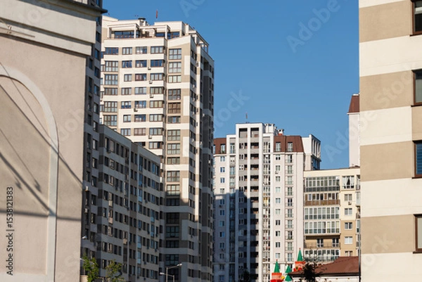 Obraz City view on a sunny day. Modern building and houses against the blue sky.