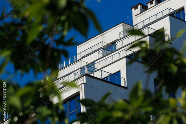 Obraz City view on a sunny day. Modern building and houses against the blue sky.