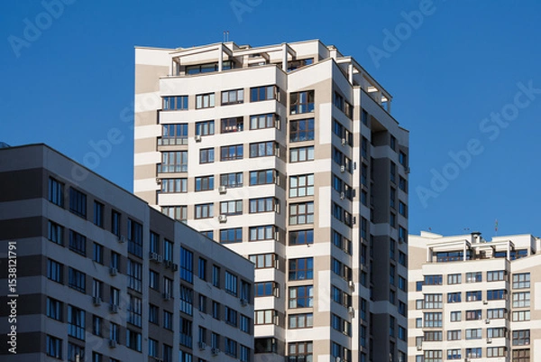 Obraz City view on a sunny day. Modern building and houses against the blue sky.