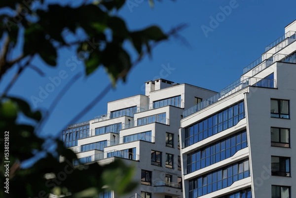 Obraz City view on a sunny day. Modern building and houses against the blue sky.