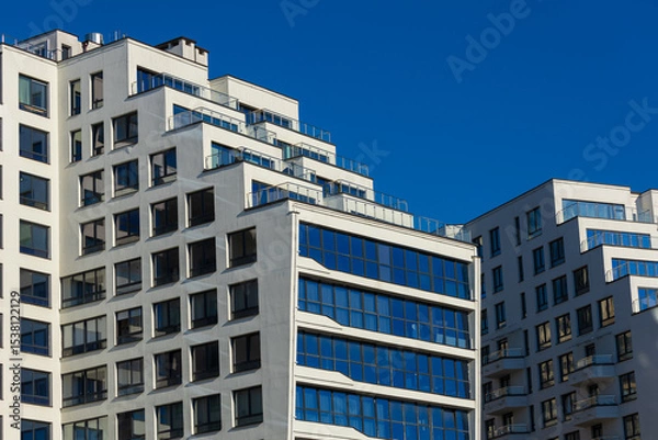 Obraz City view on a sunny day. Modern building and houses against the blue sky.