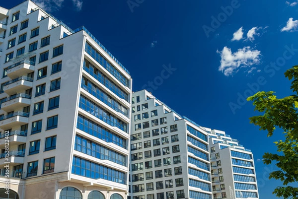 Obraz City view on a sunny day. Modern building and houses against the blue sky.