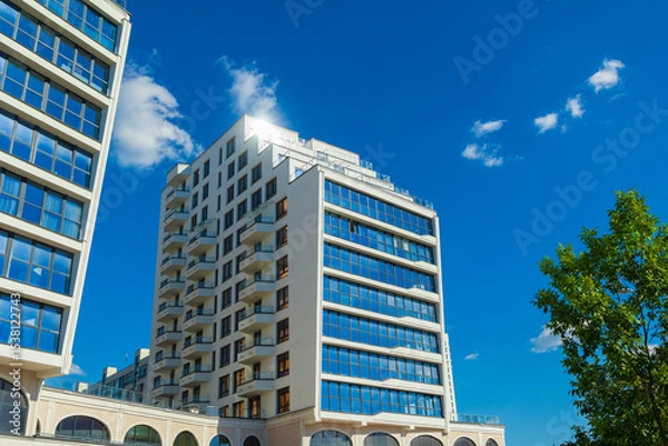 Obraz City view on a sunny day. Modern building and houses against the blue sky.