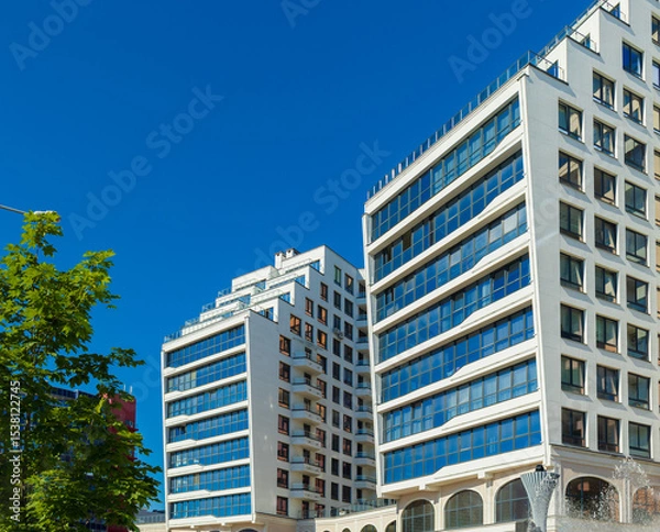 Obraz City view on a sunny day. Modern building and houses against the blue sky.