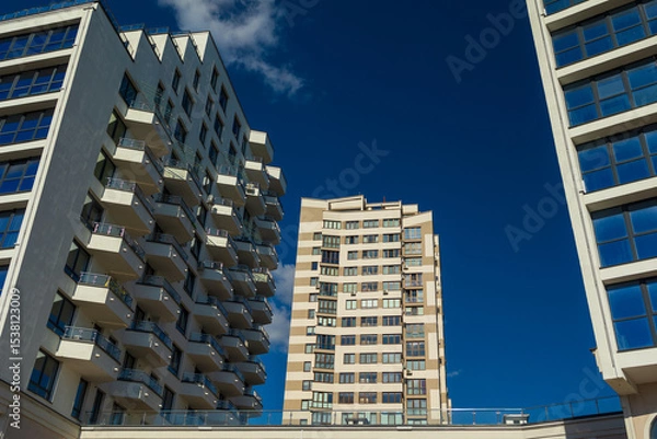 Obraz City view on a sunny day. Modern building and houses against the blue sky.